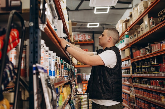 Smiling handsome salesman standing with arms crossed while making eye contact against rack at hardware store