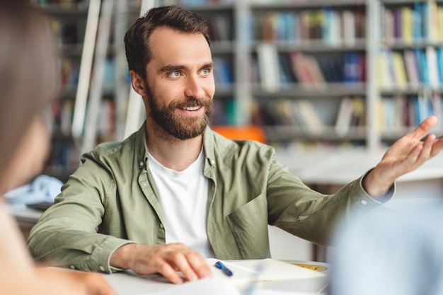 Smiling handsome worker wearing beard and casual clothes sitting at desk explaining gesturing