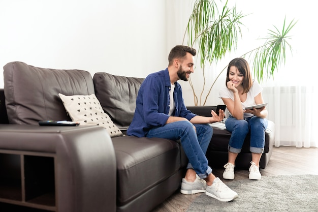 Smiling handsome young guy showing smartphone screen while sharing internet news with girlfriend at home