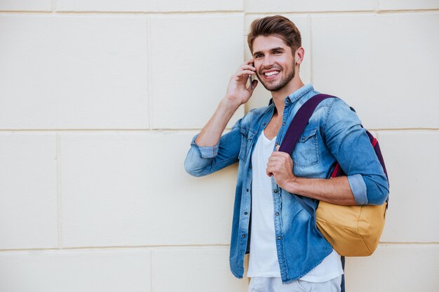 Smiling handsome young man with backpack standing and talking on mobile phone