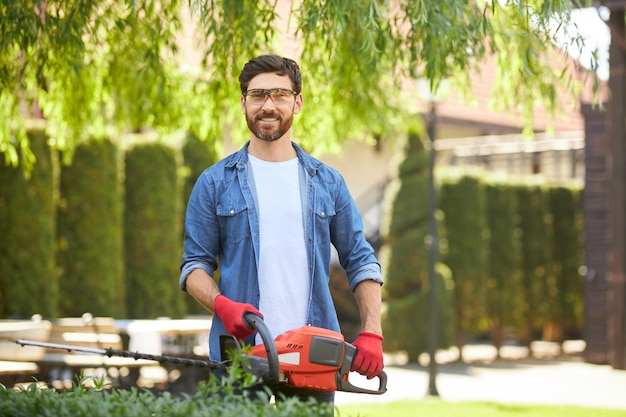Photo smiling handyman in casual clothes looking at camera while working in garden portrait of bearded