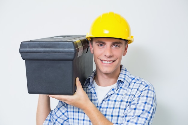 Smiling handyman in yellow hard hat carrying toolbox