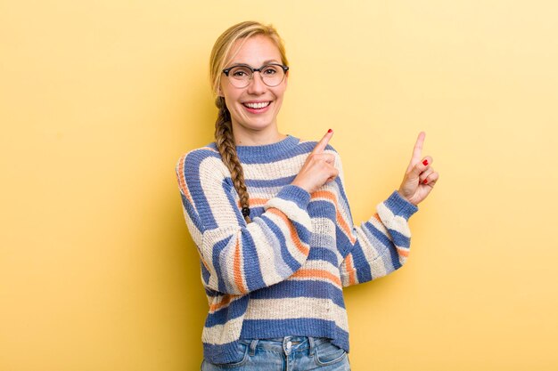 Smiling happily and pointing to side and upwards with both hands showing object in copy space