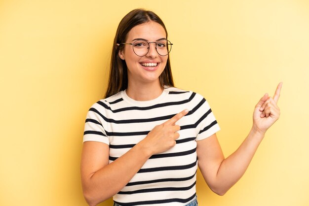 Photo smiling happily and pointing to side and upwards with both hands showing object in copy space