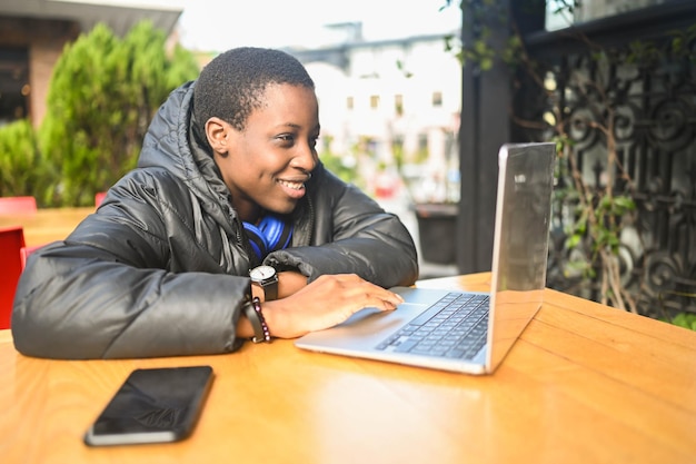 Sorridendo felice studentessa africana nera dai capelli corti in piumino nero con cuffie blu