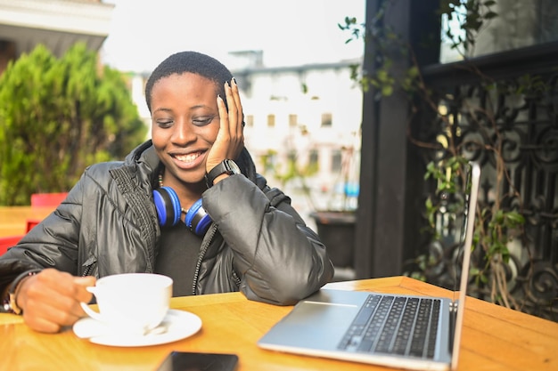 Smiling happy african black shorthaired woman student in black down jacket with blue headphones