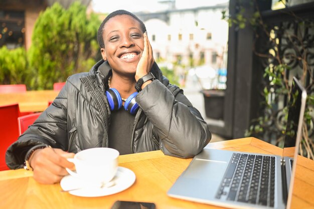 Smiling happy african black shorthaired woman student in black down jacket with blue headphones