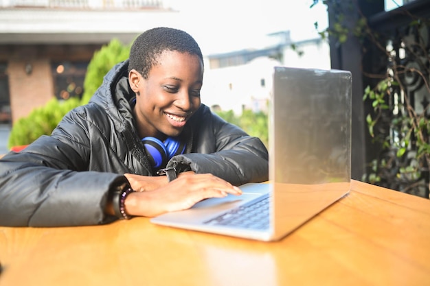 Sorridendo felice studentessa africana nera dai capelli corti in piumino nero con cuffie blu