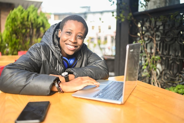 Smiling happy african black shorthaired woman student in black down jacket with blue headphones