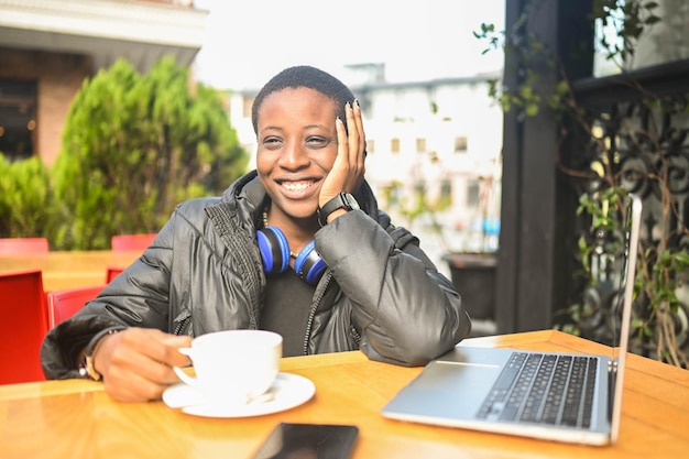 Sorridendo felice studentessa africana nera dai capelli corti in piumino nero con cuffie blu