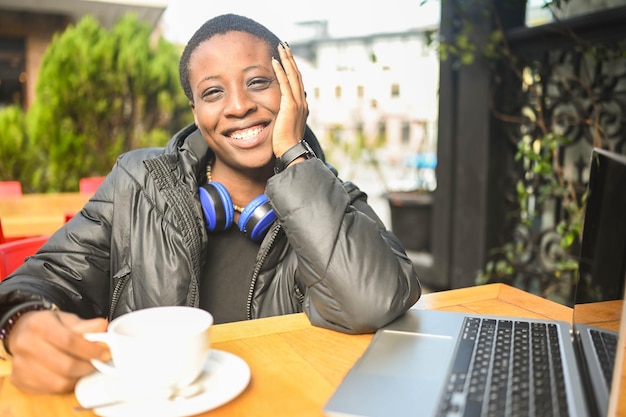 Smiling happy african black shorthaired woman student in black down jacket with blue headphones