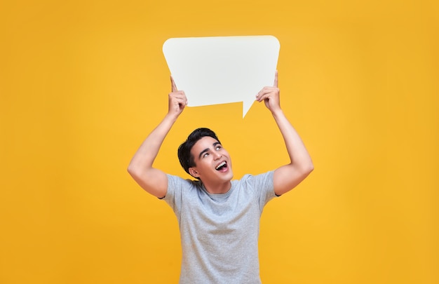 Smiling happy Asian man holding blank speech bubbles on yellow background.