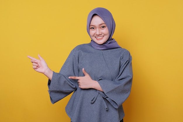 Улыбающаяся счастливая азиатская женщина в хиджабе с указательным пальцем изолирована на светло-желтом фоне баннера