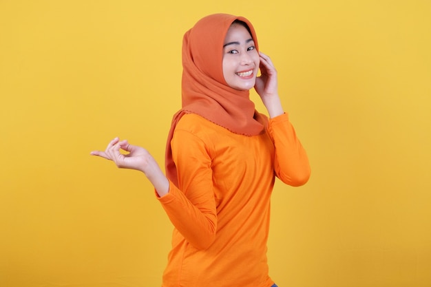 Smiling happy asian woman with her finger pointing isolated on light yellow banner background wearing hijab