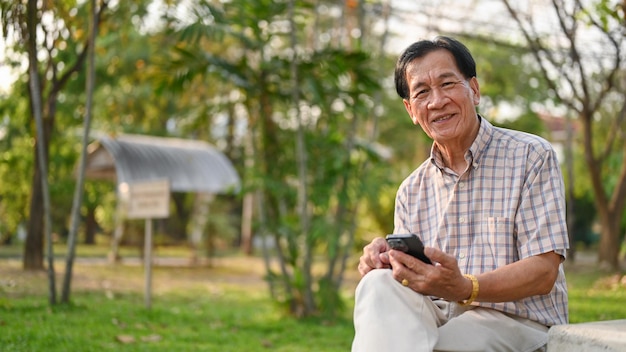 Sorridente e felice uomo in pensione asianaged tiene il suo smartphone e si rilassa nel cortile