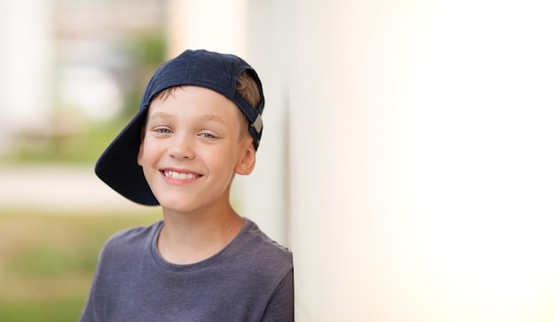 A smiling happy boy with crooked teeth is standing against the wall