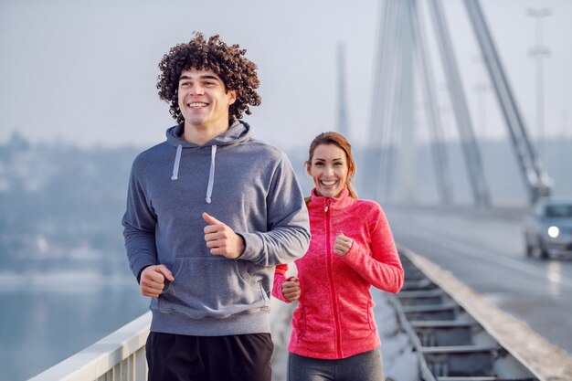 Foto coppie caucasiche felici sorridenti in abiti sportivi che corrono sul ponte. orario invernale. concetto di fitness all'aperto.