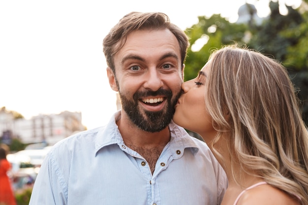 smiling happy cheery young loving couple walking by street outdoors kissing