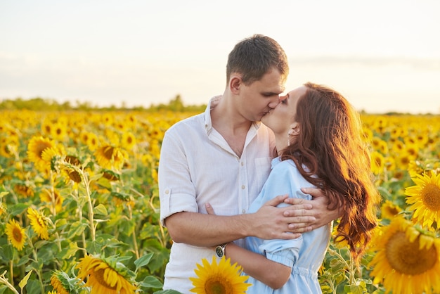 Smiling happy couple hugging in the middle of a field with sunflowers. Sun glare. Romantic Couple on a Love Moment.