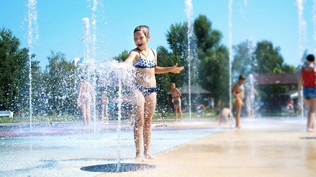 Smiling happy eight year old girl in swimsuit having fun in splashes in street city fountain