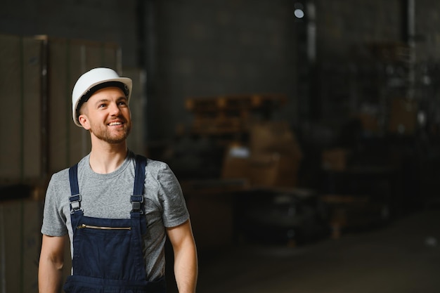 Smiling and happy employee industrial worker indoors in factory\
young technician with white hard hat