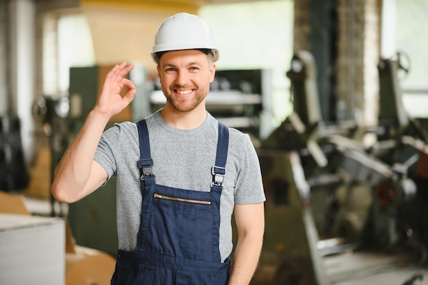 Smiling and happy employee Industrial worker indoors in factory Young technician with white hard hat