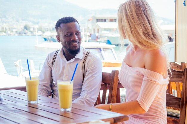 Smiling happy european woman in straw hat and sexy pink dress walking with afro american ethnic man by summer beach with rock view in Turkey tropical resort