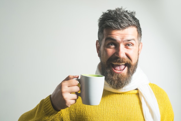 セーターでマグカップ笑顔の男とコーヒーティー水を飲む笑顔と幸せなハンサムなひげを生やした男と