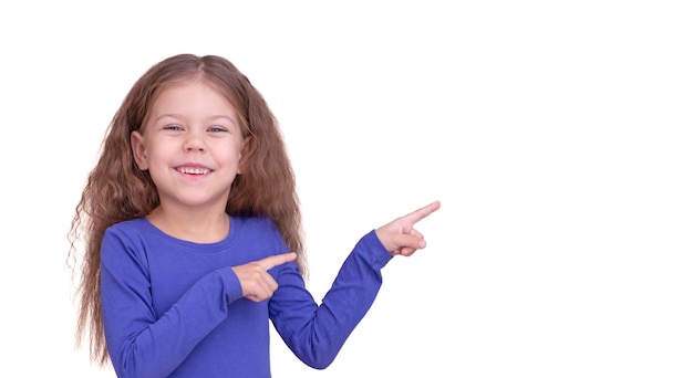 Улыбающаяся и счастливая маленькая девочка показывает указательными пальцами на копировальное пространство