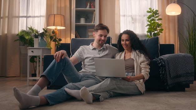 Smiling happy love couple family Caucasian man guy male with Hispanic woman Latina girl female together at home shopping online buy purchase win success using laptop high five cooperation teamwork