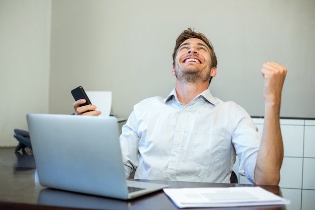 オフィスで携帯電話を保持している笑顔の幸せな男