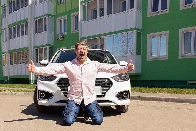 Un uomo sorridente e felice è in piedi accanto a una nuova auto gesti acquisto e noleggio di un'auto