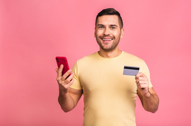 smiling happy man wearing casual tshirt holding smartphone and plastic credit card