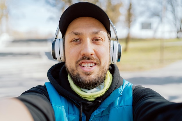 A smiling happy man wearing wireless headphones takes a selfie during a morning workout run