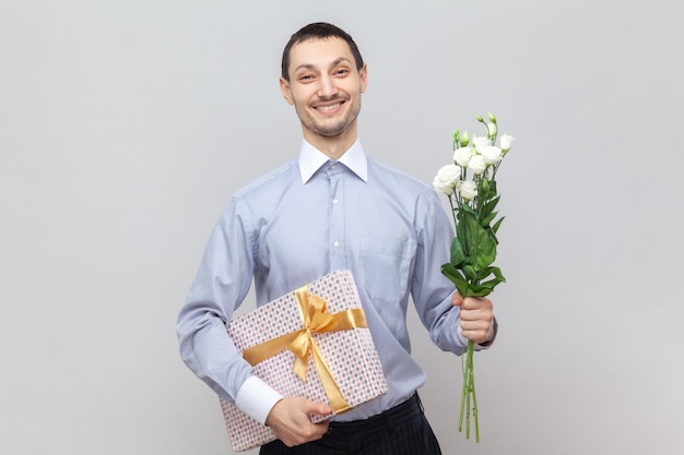 Photo smiling happy man with present box and bouquet of flowers congratulate her girlfriend with birthday