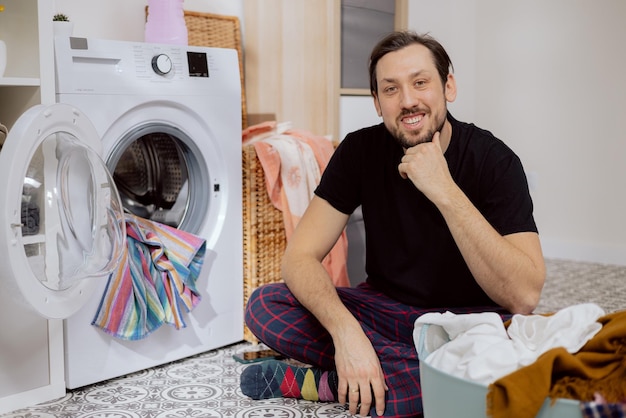 Smiling happy men sitting on the laundry room floor next to the washing machine