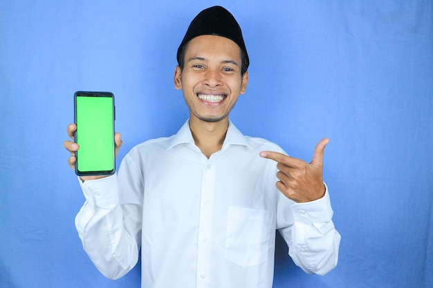 写真 空の電話画面を表示する帽子をかぶったアジア人イスラム教徒の笑顔 広告コンセプト