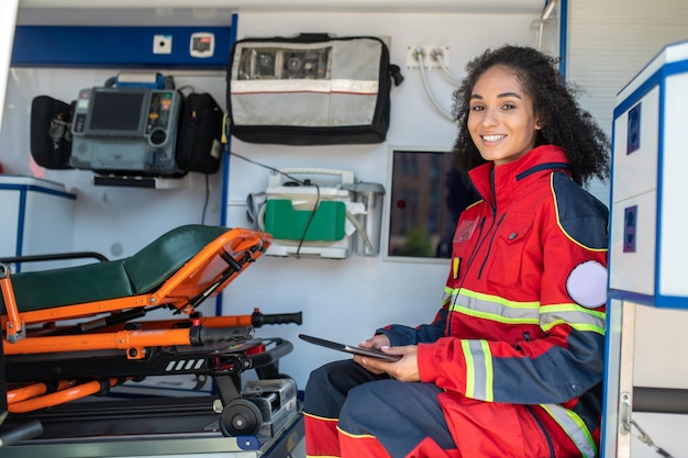 Photo smiling happy paramedic with the tablet in her hands sitting in the medical emergency vehicle