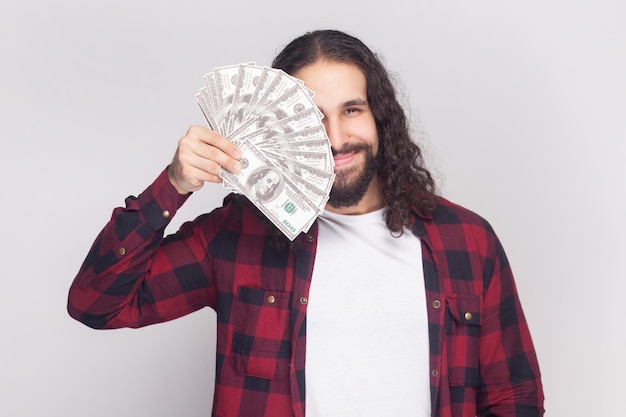 Smiling happy positive bearded man covering half of face with dollar banknotes