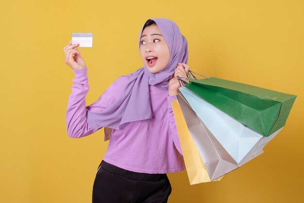 Smiling happy pretty girl using credit card to waste some money in mall, holding shopping bags, buy gifts or presents, treat yourself day