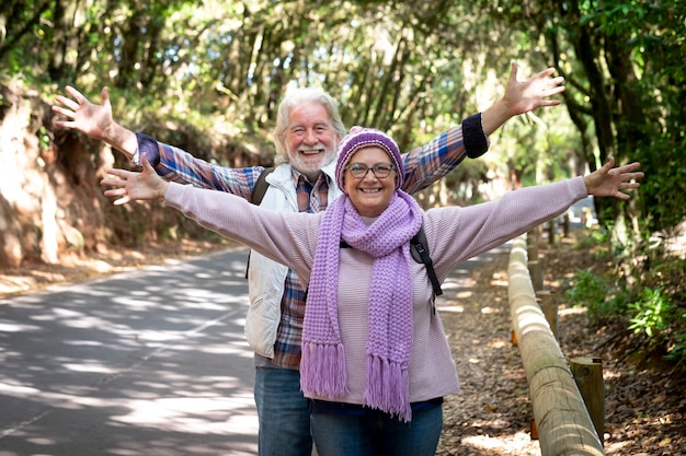 Sorridente coppia senior felice con le braccia alzate che guarda l'obbiettivo godendo escursione in montagna in una giornata invernale. anziani in pensione attivi e concetto di divertimento