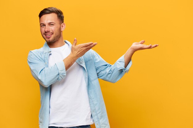 Smiling happy tanned handsome man in blue basic tshirt hold\
invisible object near head posing isolated on orange yellow studio\
background copy space banner mockup people emotions lifestyle\
concept