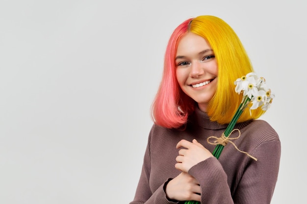 Smiling happy trendy teenager girl with bouquet of white daffodils flowers on light background