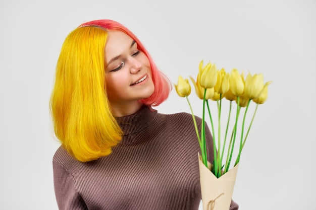 Smiling happy trendy teenager girl with bouquet of yellow tulips on light background, winter spring season