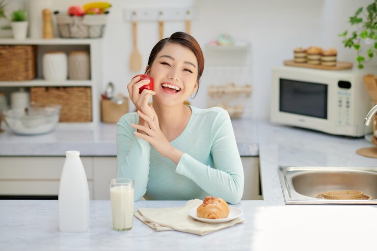 Photo キッチンに座って朝食に新鮮なリンゴを食べる幸せな女の笑顔