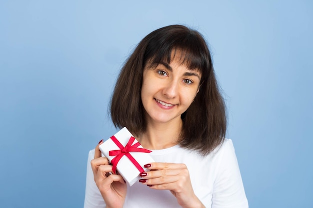 青い背景に分離されたギフトボックスを保持している幸せな女の笑顔。バレンタインデーや誕生日のコンセプト