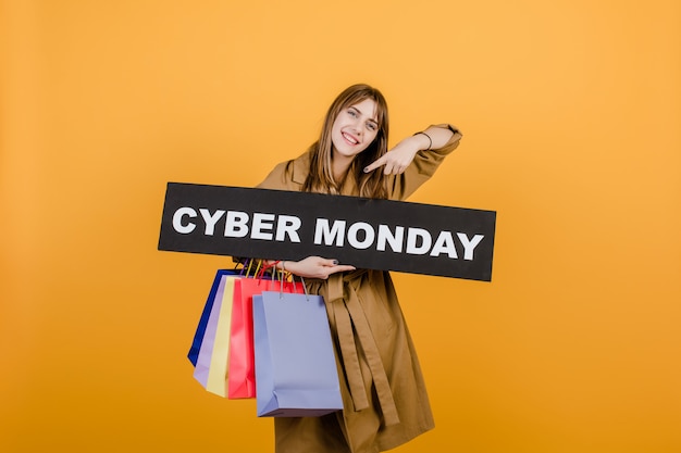 Smiling happy woman with cyber monday sign and colorful shopping bags isolated over yellow