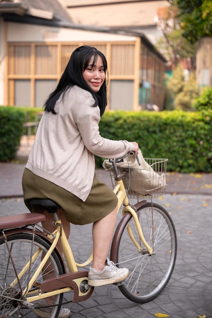 A smiling happy young Asian woman in a cute dress is riding a bicycle in the city