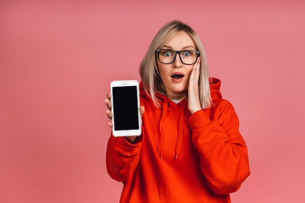 Smiling happy young blonde woman showing tablet computer screen isolated over pink background.