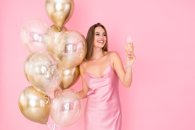 Smiling happy young woman raises up glass of champagne holds golden air balloons celebration